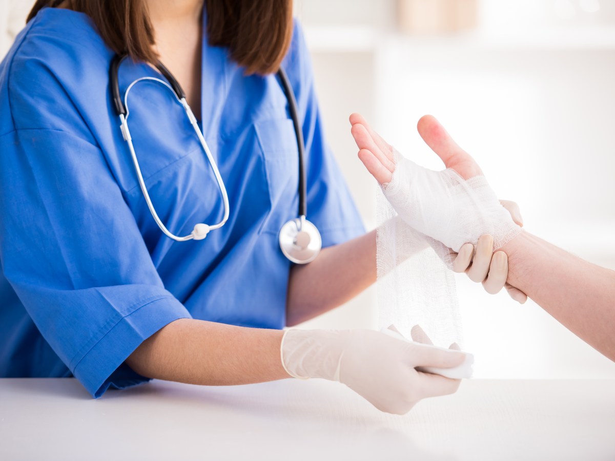 Nahaufnahme einer Ã„rztin bandagiert die Hand eines Patienten beziehungsweise einer Patientin.