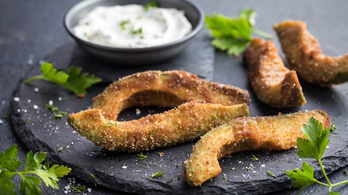 Frittierte Avocado auf schwarzem Teller mit KrÃ¤uter-Dip.