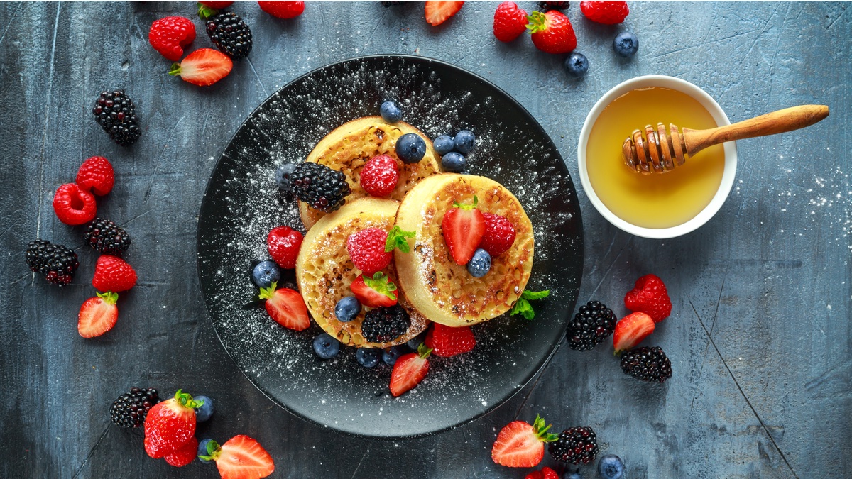 Englische Crumpets auf einem schwarzen Teller und Obst.