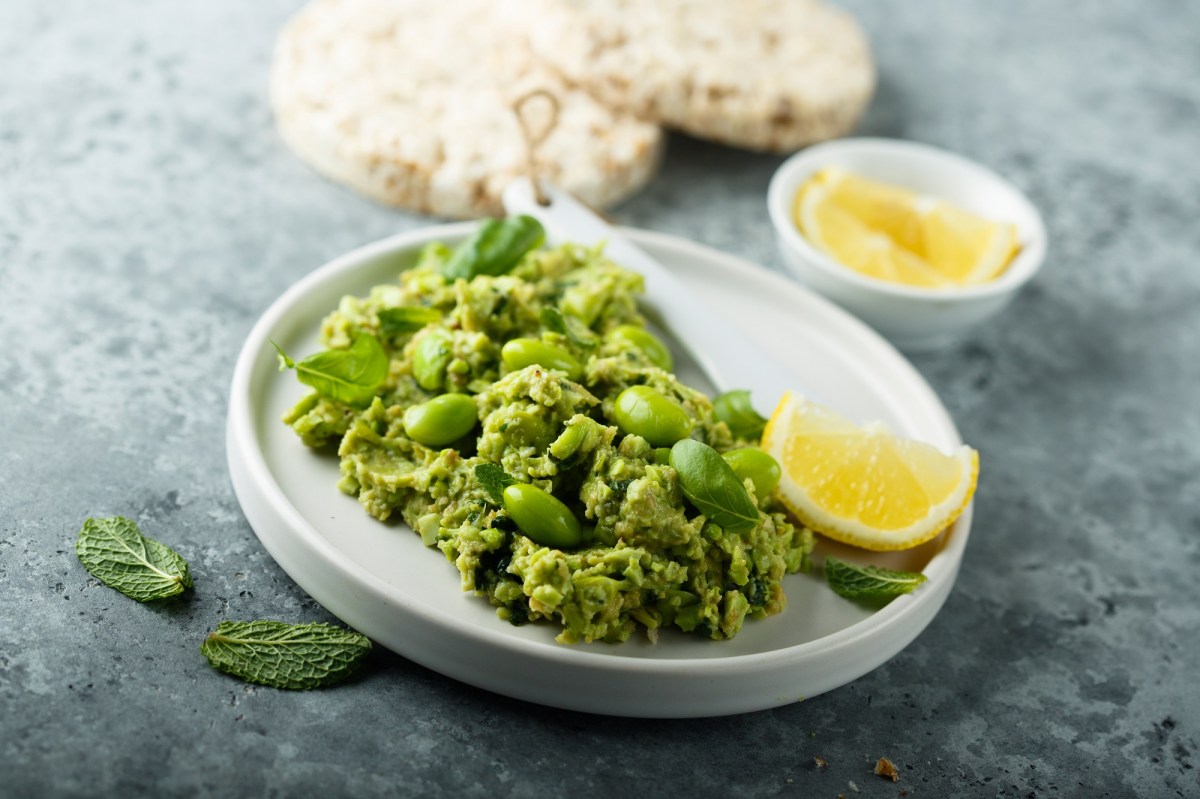 Edamame-Guacamole, mit etwas Minze garniert, auf einem weiÃŸen Teller. Serviert mit Pita-Brot.