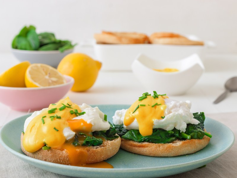 Eggs Florentine aus Spinat mit KÃ¤sesoÃŸe auf einem blauen Teller.