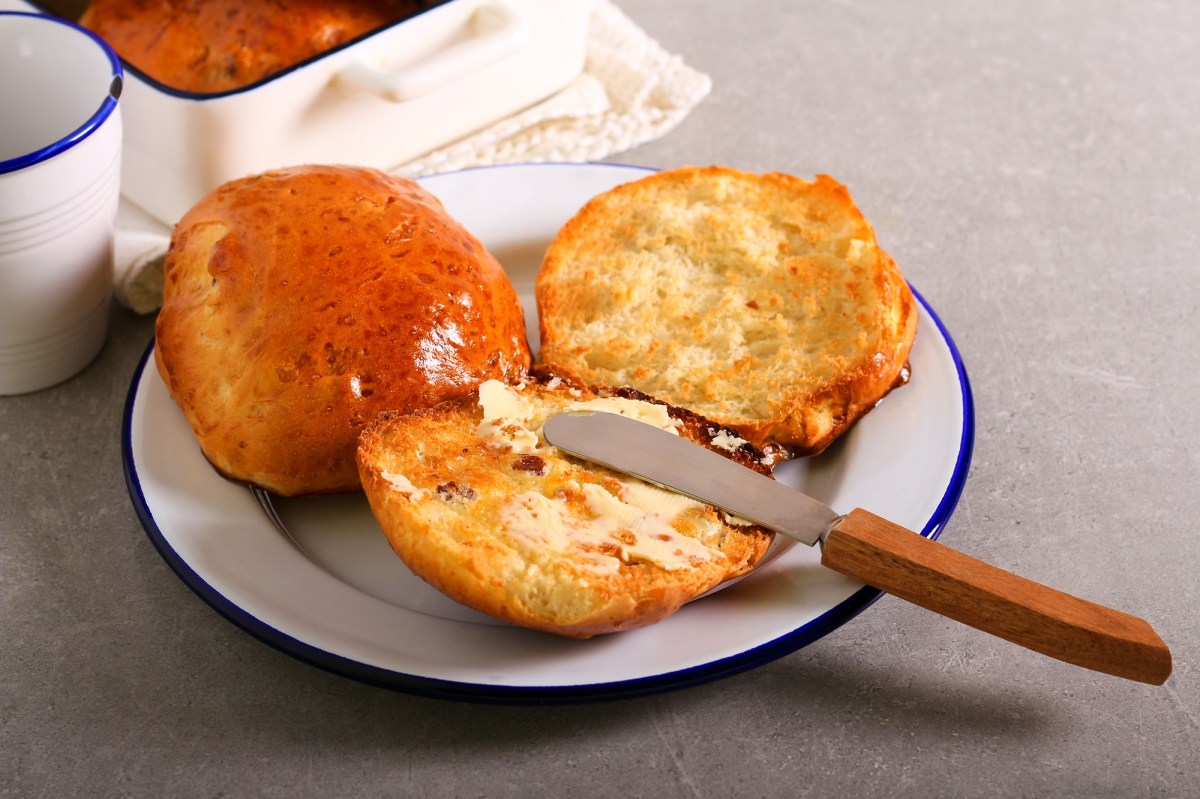 Englische Teekuchen auf einem weiÃŸen Teller mit blauem Rand. Sie sind aufgeschnitten und mit Butter bestrichen.