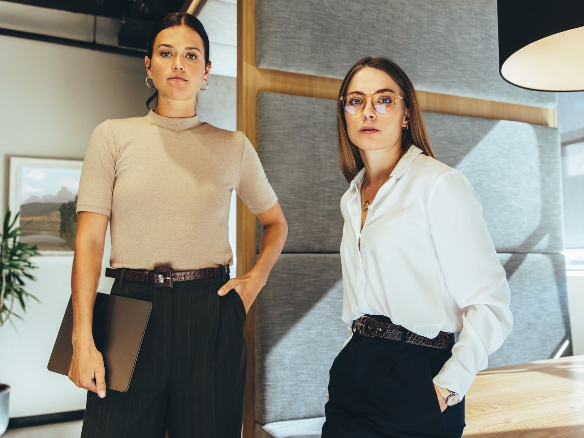 Junge GeschÃ¤ftsfrauen schauen in die Kamera, wÃ¤hrend sie in einem BÃ¼ro stehen.