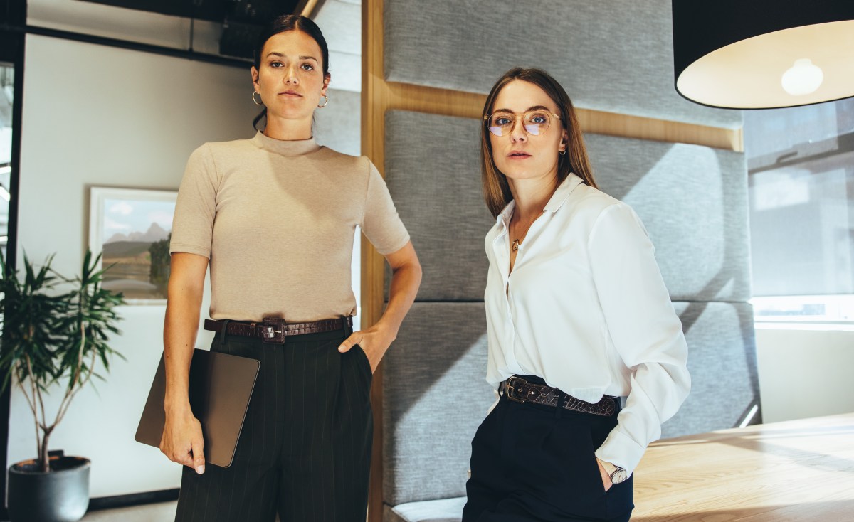 Junge GeschÃ¤ftsfrauen schauen in die Kamera, wÃ¤hrend sie in einem BÃ¼ro stehen.