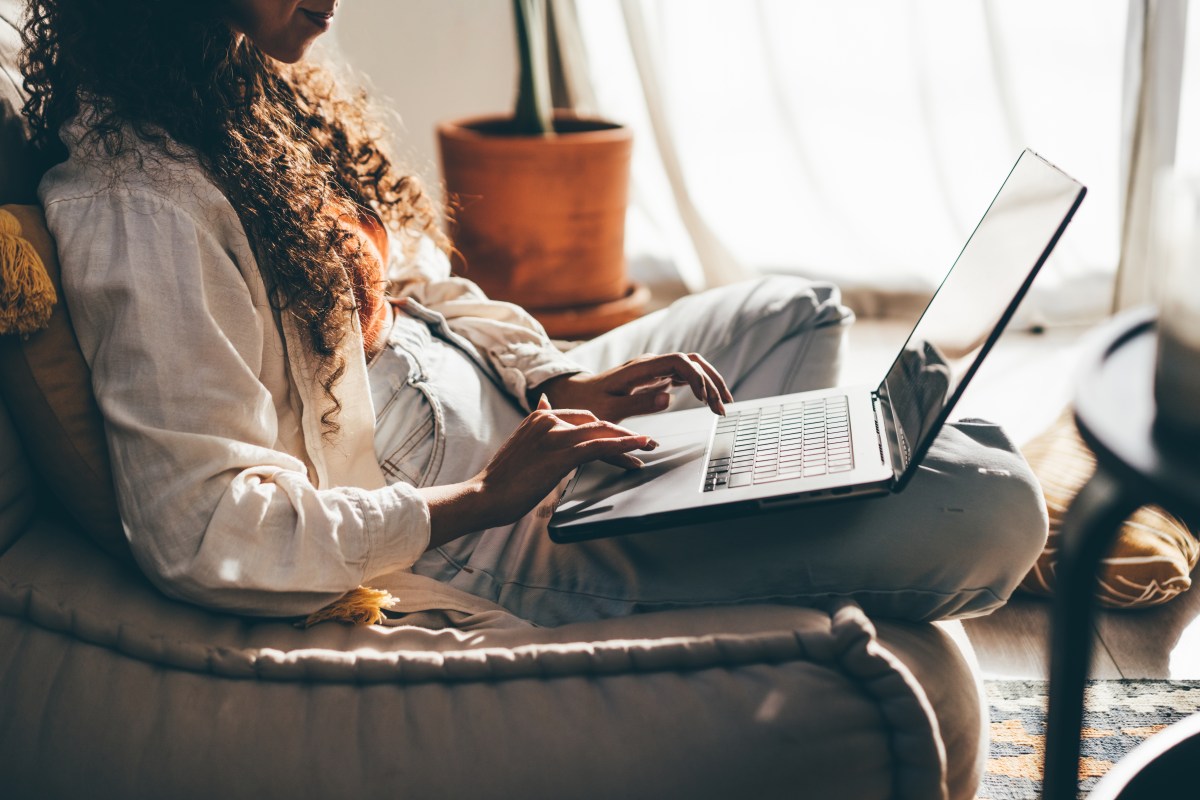 Junge Frau mit Laptop arbeitet im Wohnzimmer.