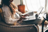 Junge Frau mit Laptop arbeitet im Wohnzimmer.