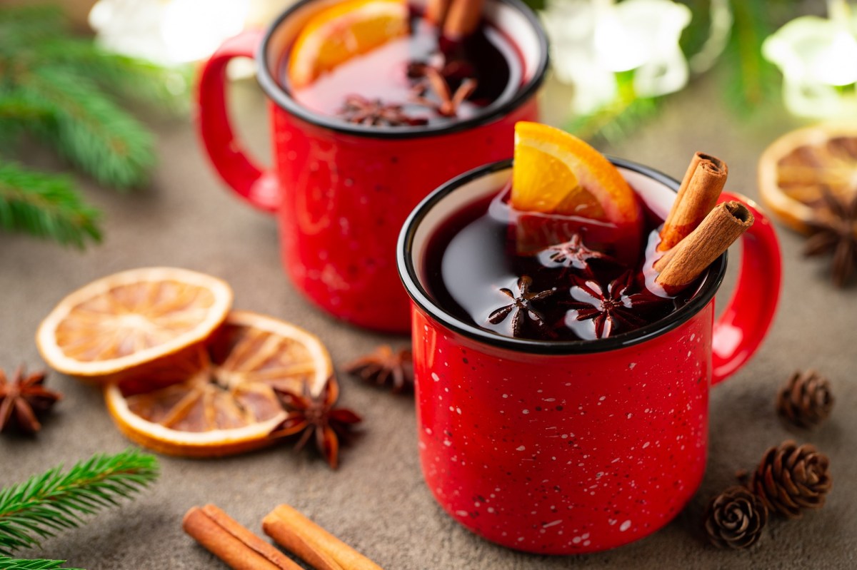 2 rote Tasse mit GlÃ¼hwein, der mit GlÃ¼hweingewÃ¼rzen wie Zimt und Anis sowie Orangenscheiben garniert ist.