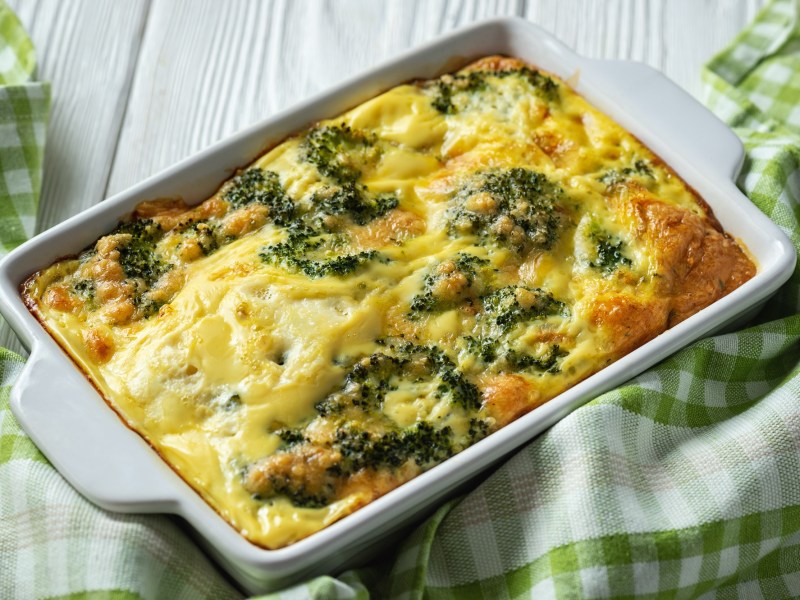 Kartoffel-Brokkoli-Gratin ohne Vorkochen in einer Auflaufform, darum ist ein grÃ¼n-weiÃŸ kariertes Geschirrtuch drapiert.