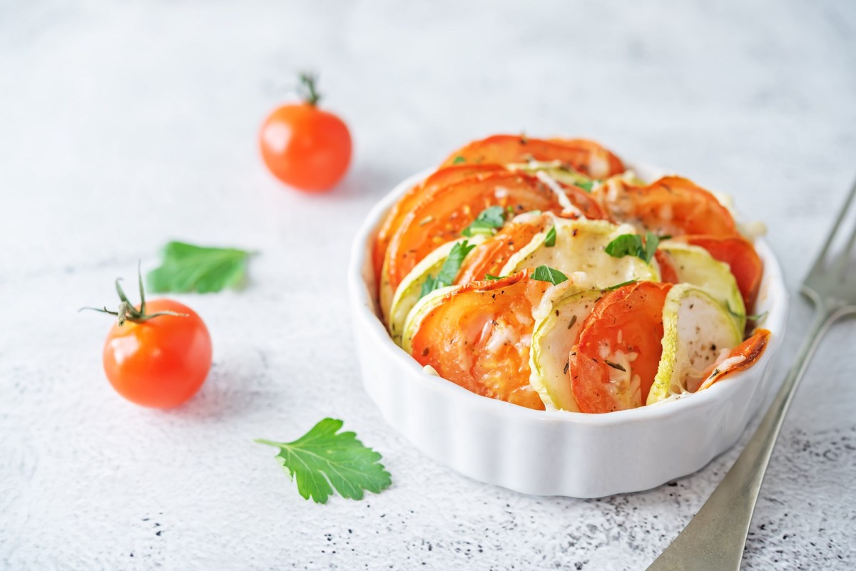 Mini-GemÃ¼se-Gratin mit Tomate und Zucchini in einer weiÃŸen runden Auflaufform, daneben Mini-Tomaten.