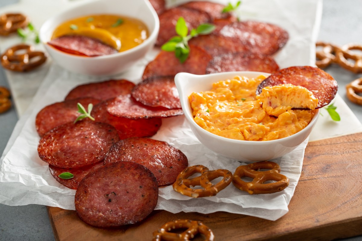 Salami-Chips mit KÃ¤sedip auf einer Serviette. Daneben liegen Salzbrezeln.