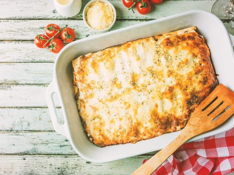 Sauerkraut-Lasagne in Auflaufform, darauf ein HolzlÃ¶ffel, drumherum Tomaten und KÃ¤se, Draufsicht.