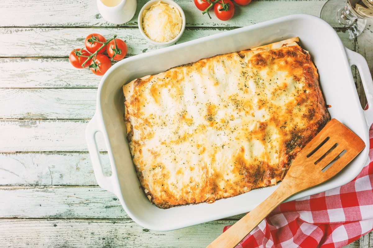 Sauerkraut-Lasagne in Auflaufform, darauf ein HolzlÃ¶ffel, drumherum Tomaten und KÃ¤se, Draufsicht.