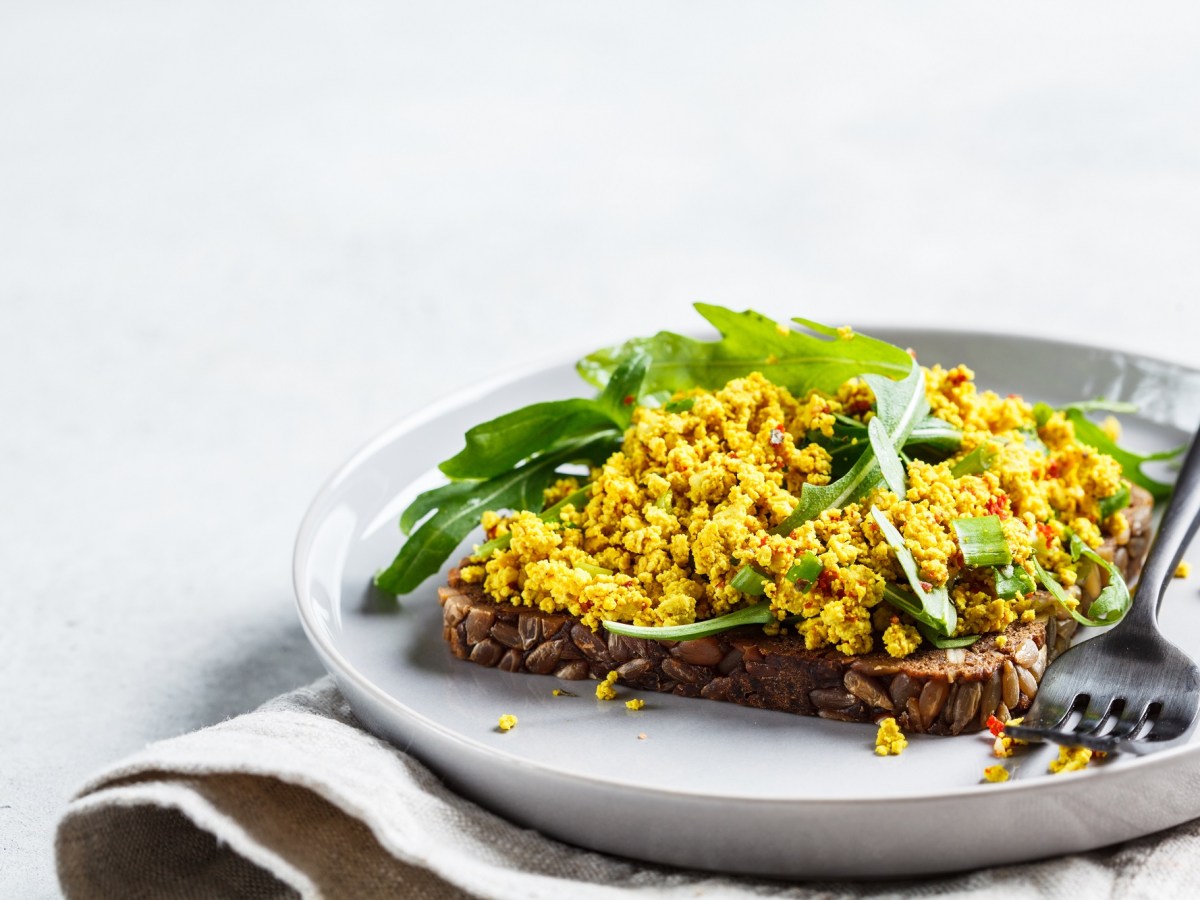 Ein Brot belegt mit veganem RÃ¼hrei und Rucola auf einem Teller, Nahaufnahme.