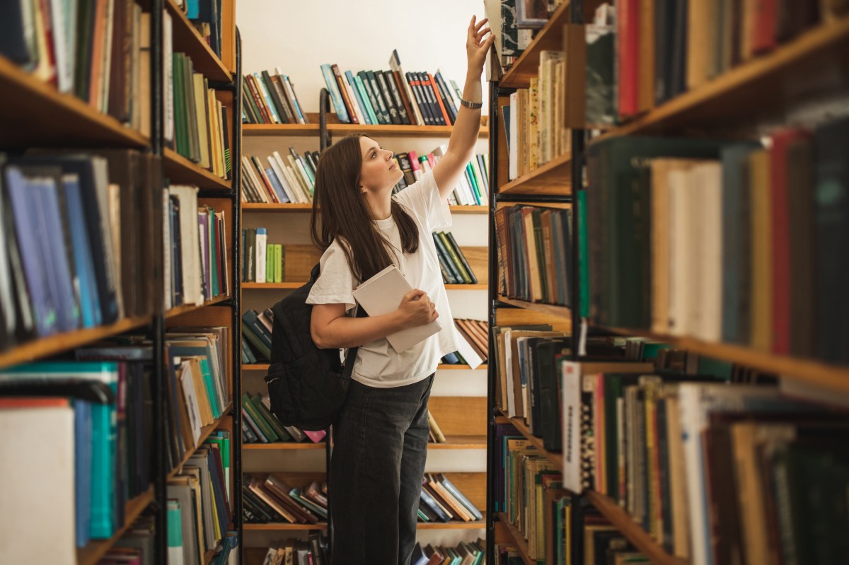 Studentin steht in der UniversitÃ¤tsbibliothek und sucht ein Buch.