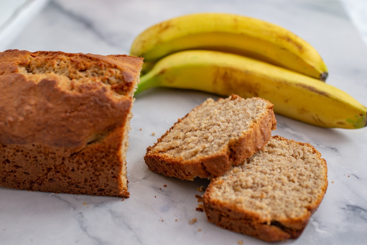 Ein angeschnittenes Bananenbrot ohne Zucker, daneben zwei Bananen.