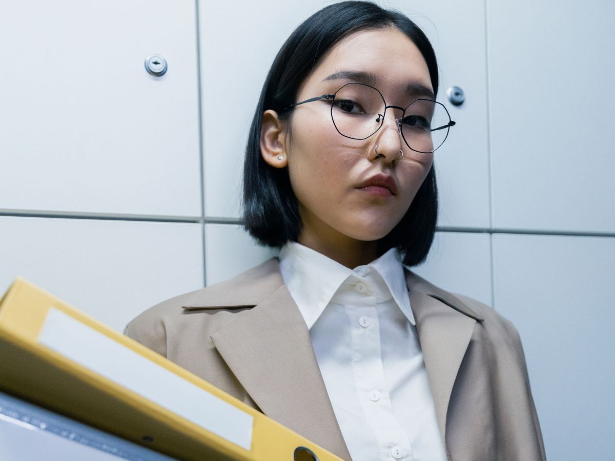 Eine Frau mit einem schwarzen Bob und Brille trÃ¤gt einen gelben Aktenordner.