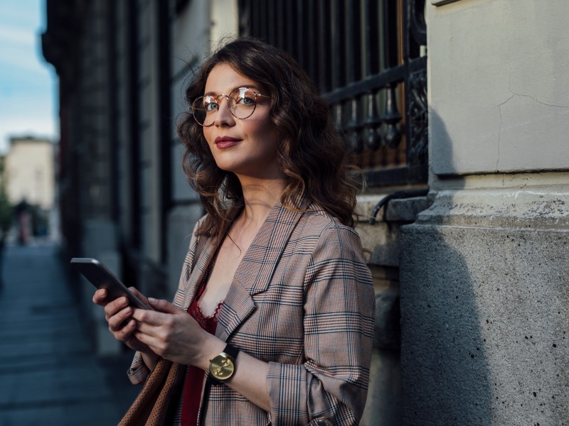 Eine elegante Frau steht auf der StraÃŸe und hÃ¤lt ihr Telefon in der Hand.