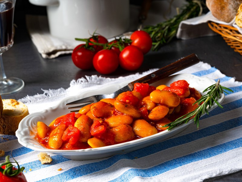 dicke Bohnen in TomatensoÃŸe auf einem ovalen Teller.