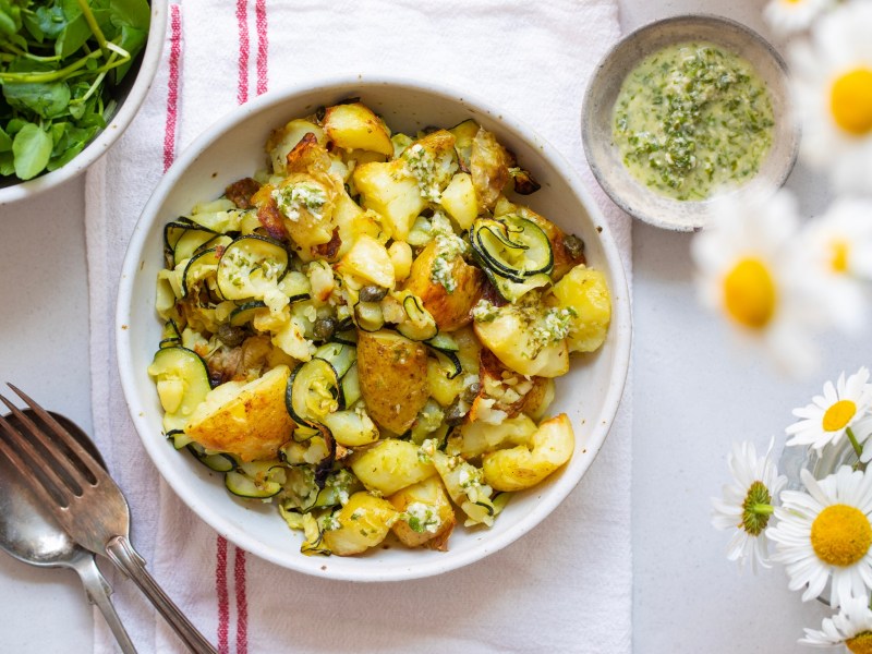 Kartoffelsalat mit gegrillter Zucchini in einer weiÃŸen Schale. Daneben steht eine Schale mit Dressing.