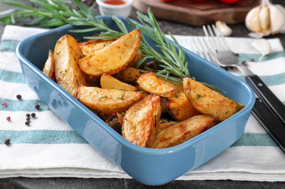 Eine Auflaufform mit Kartoffelspalten mit Knoblauch und Rosmarin auf einem blau-weiÃŸ gestreiften Geschirrtuch.