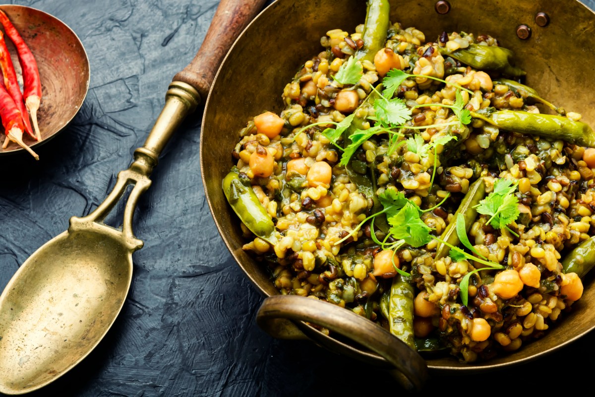 Kitchari, indischer Kokosreis mit Bohnen und Kichererbsen, in einer BlechschÃ¼ssel, daneben ein LÃ¶ffel. Draufsicht.