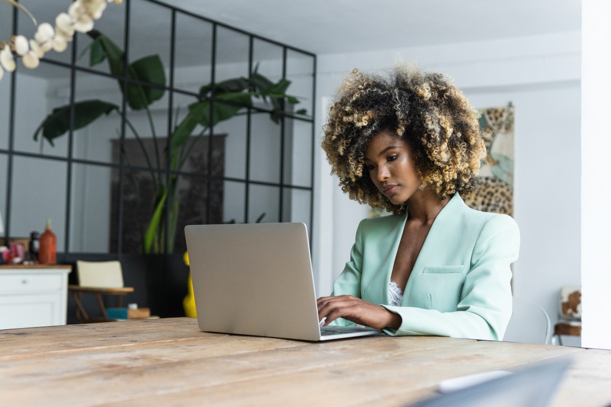 Eine Frau mit Afro sitzt an einem Tisch und arbeitet am Laptop.