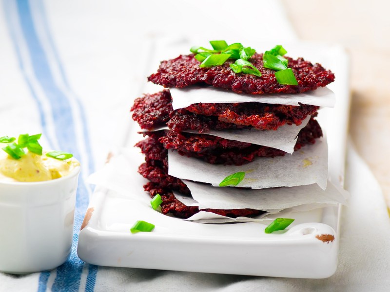 Ein Stapel Rote-Bete-Puffer auf einer weiÃŸen Unterlage, getrennt von kleinen StÃ¼cken Backpapier.