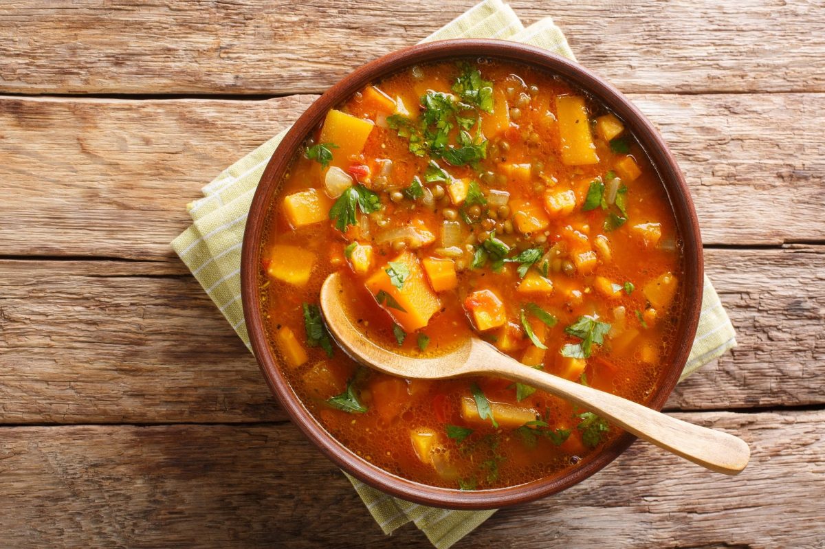 Eine SchÃ¼ssel SÃ¼ÃŸkartoffel-Curry-Suppe mit HolzlÃ¶ffel in der Draufsicht.