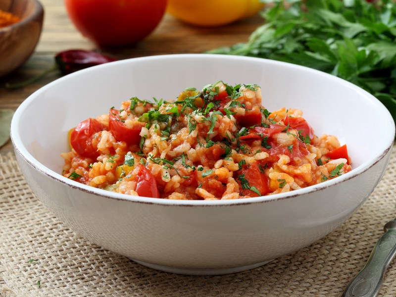 Eine SchÃ¼ssel Tomatenreis mit Spinat, dahinter frische Zutaten.