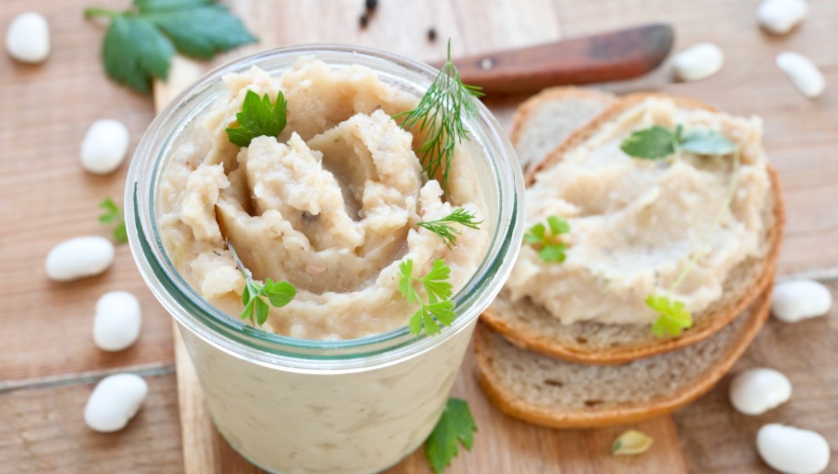 WeiÃŸe-Bohnen-Aufstrich im Glas. Daneben eine Scheibe Brot mit Aufstrich.