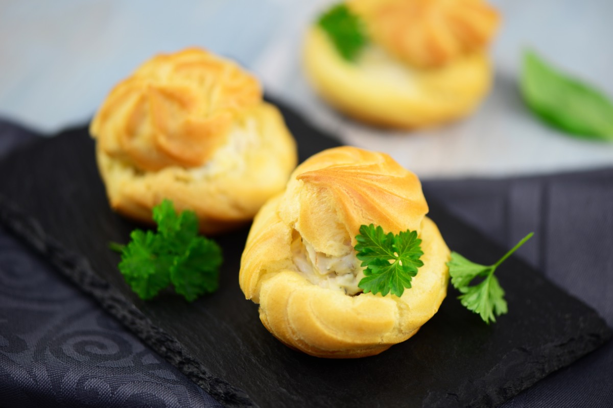 Drei Windbeutel mit FrischkÃ¤se-FÃ¼llung auf einer Schiefertafel. Garniert sind sie mit Petersilie.