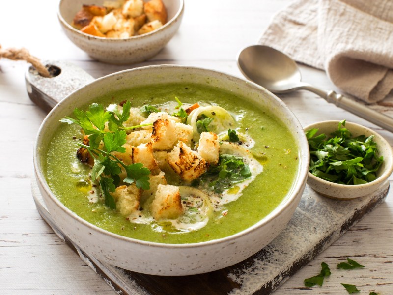 Eine SchÃ¼ssel Zucchini-Spinat-Suppe mit CroÃ»tons, Lauch, Schmand und KrÃ¤utern.