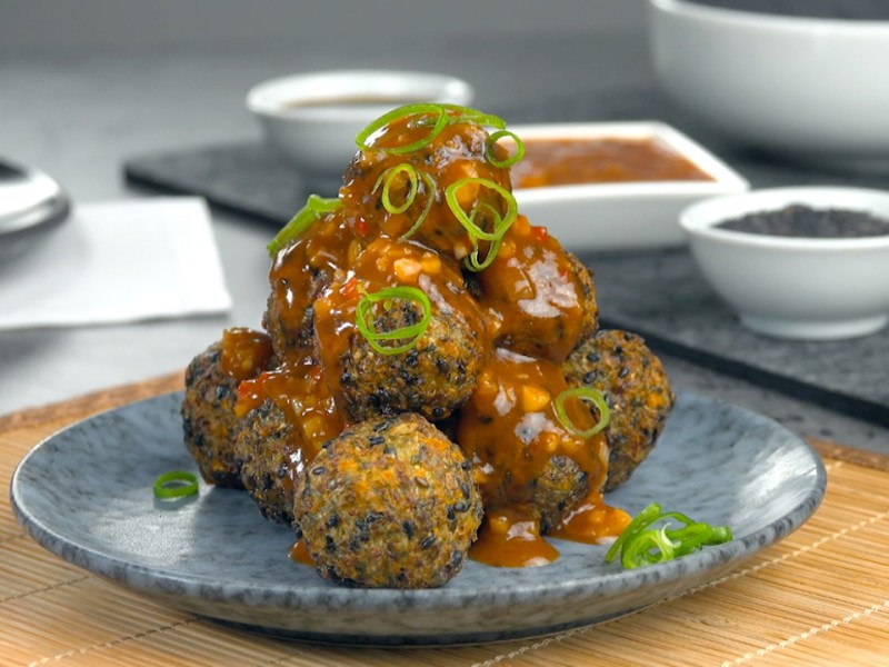 Eine Pyramide aus frittierten GemÃ¼sebÃ¤llchen mit Spitzkohl und schwarzen Sesamauf einem Teller.