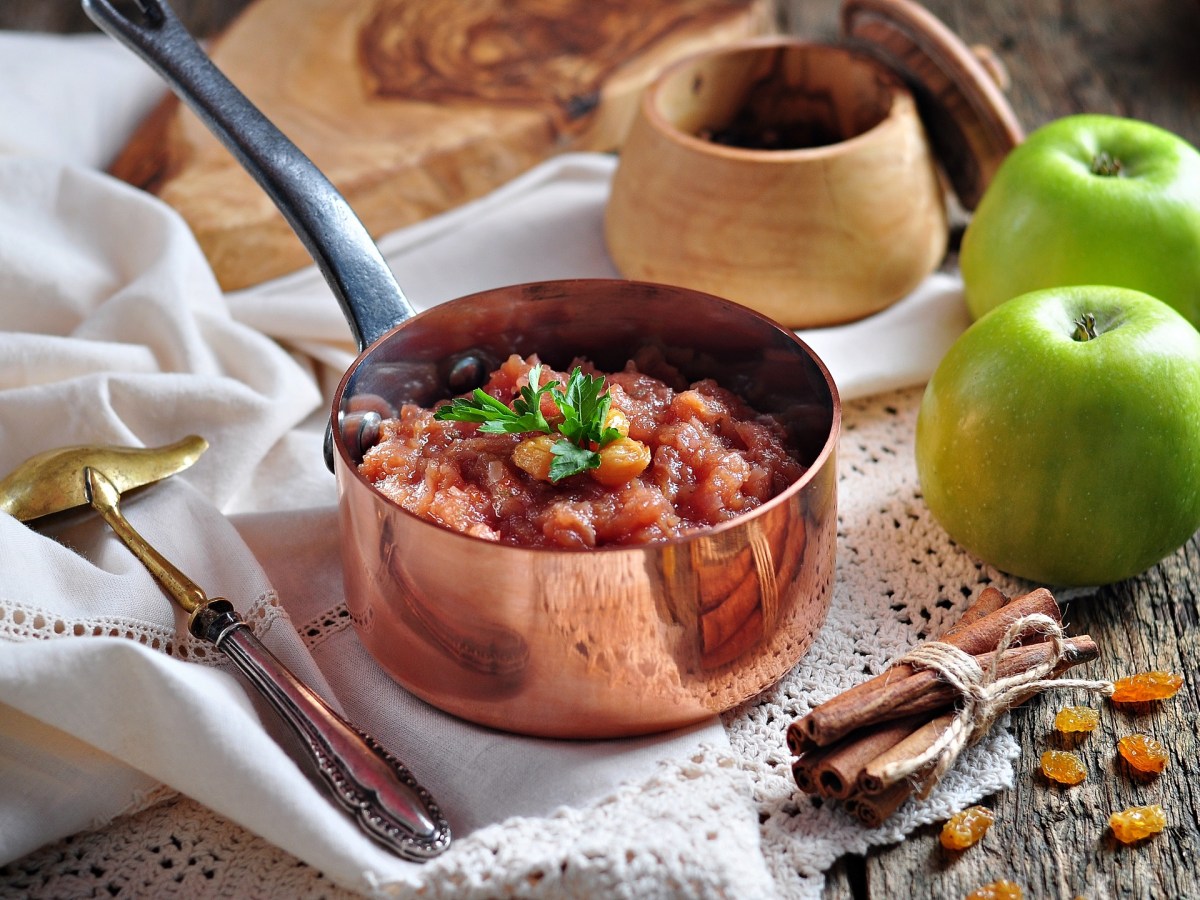 Ein kleiner Topf mit Apfelchutney und Rosinen, drumherum frische grÃ¼ne Ã„pfel, Sultaninen und ZubehÃ¶r.