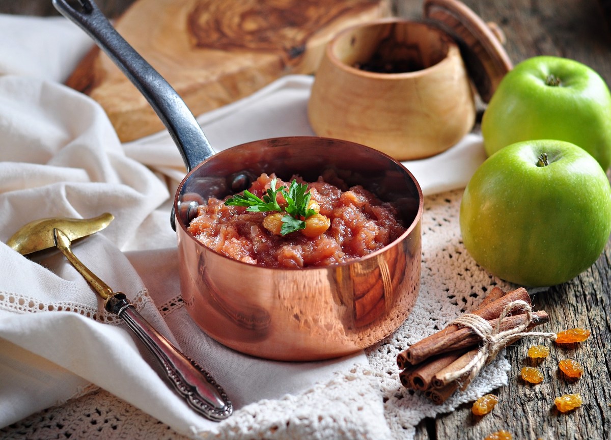 Ein kleiner Topf mit Apfelchutney und Rosinen, drumherum frische grÃ¼ne Ã„pfel, Sultaninen und ZubehÃ¶r.