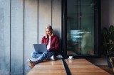 Eine junge Frau in einem lÃ¤ssigen Outfit lÃ¤chelt, wÃ¤hrend sie ihren Laptop an einem gemÃ¼tlichen Fensterplatz im CafÃ© benutzt.