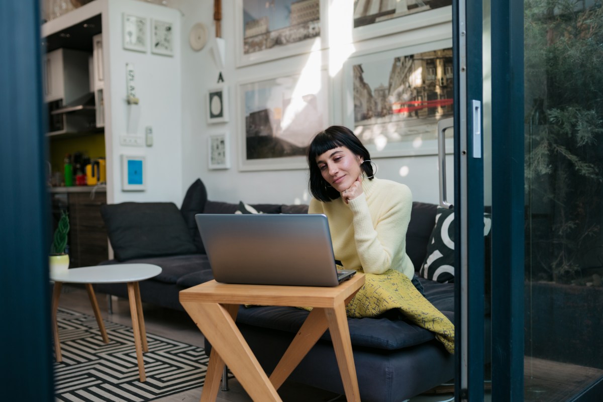 Junge Frau arbeitet bequem von ihrer Wohnung aus mit einem Laptop.