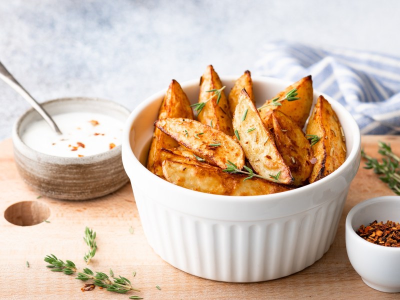 Eine weiÃŸe Schale Kohlrabi-Wedges auf einem Brett, auf dem auch einige weitere SchÃ¼sseln mit Dips stehen.