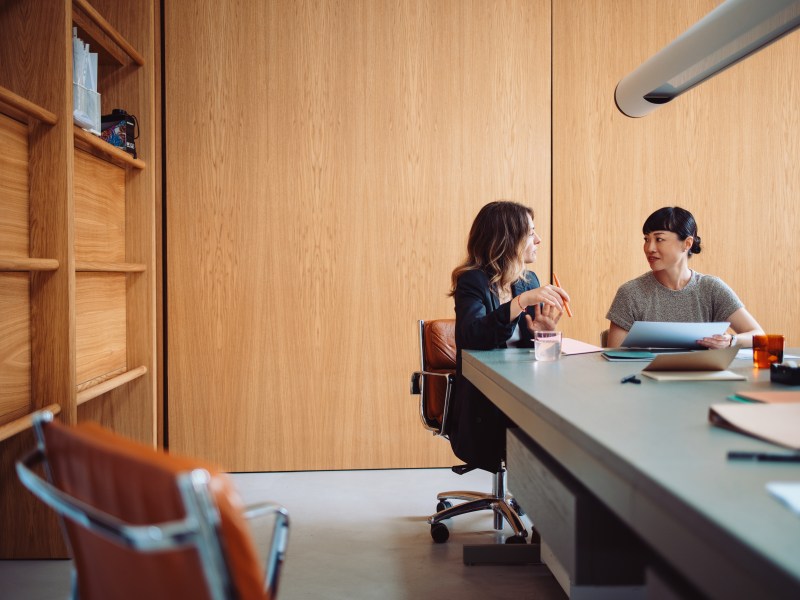 Zwei Frauen fÃ¼hren ein GesprÃ¤ch an einem BÃ¼rotisch.