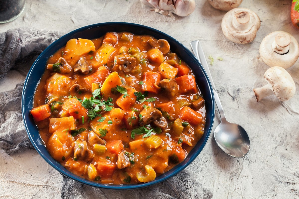 Ein Teller Pilzgulasch mit MÃ¶hren und Sellerie, daneben ein LÃ¶ffel und Pilze, Draufsicht.