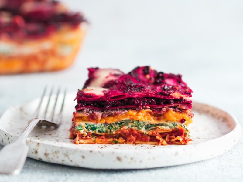 Ein StÃ¼ck vegane Regenbogen-Lasagne auf einem Teller. Der Rest ist im Hintergrund zu sehen.