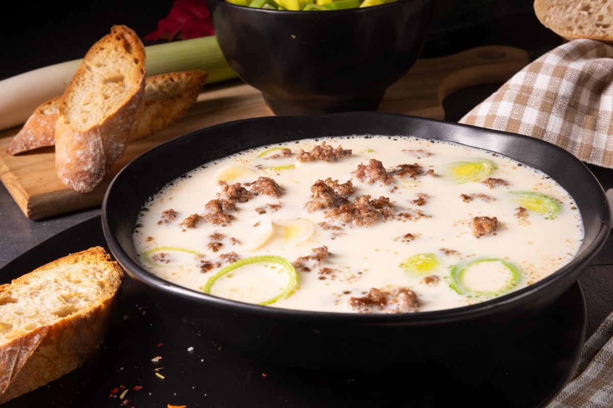 Eine SchÃ¼ssel vegane KÃ¤se-Lauch-Suppe mit Hack, daneben gerÃ¶stete Baguettescheiben.