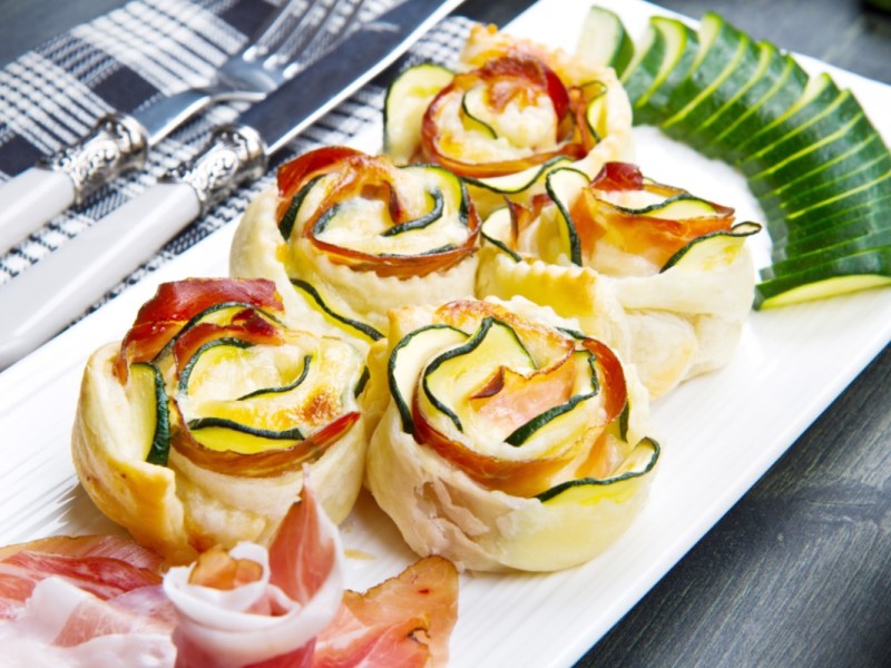 FÃ¼nf Zucchini-BlÃ¤tterteig-Rosen auf einer eckigen Servierplatte.