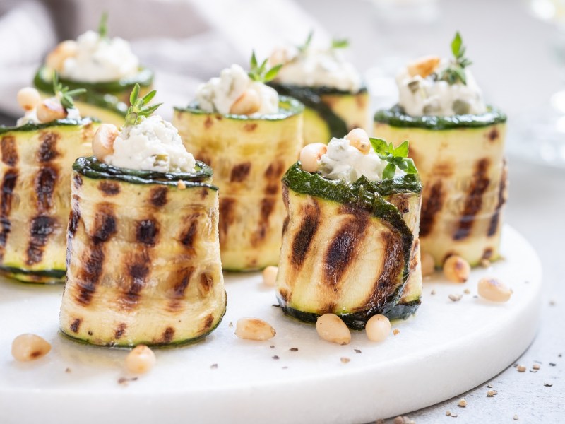 Zucchini-RÃ¶llchen mit FrischkÃ¤se auf einem Tablett.