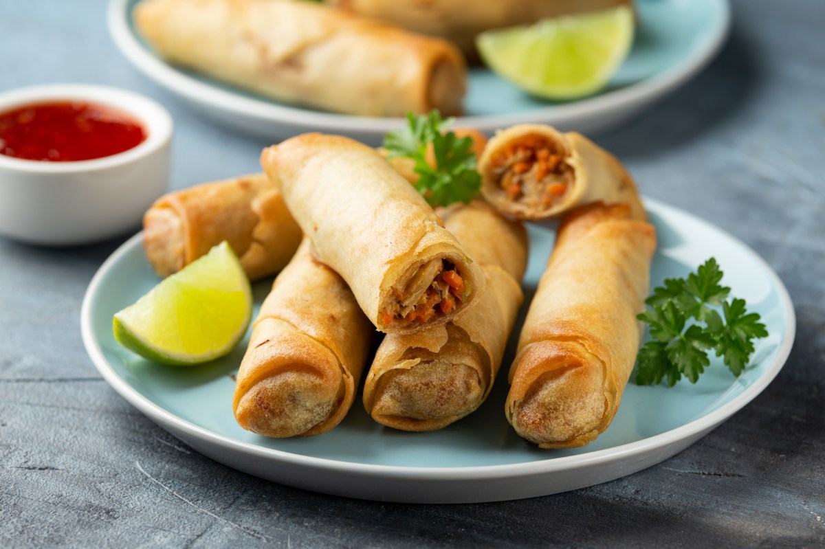 Kimchi-FrÃ¼hlingsrollen liegen auf einem hellblauen Teller. Sie sind mit einem LimettenstÃ¼ck und frischer Petersilie garniert. Im Hintergrund steht eine Schale mit SoÃŸe, sowie ein weiterer Teller FrÃ¼hlingsrollen.