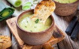 Eine Schale mit veganer Lauch-Pastinaken-Suppe, in der ein StÃ¼ck kross gebackenes Brot steckt.