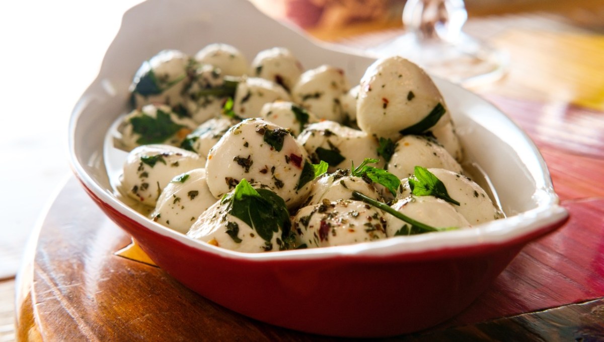 Eine rote Schale voller mariniertem Mozzarella mit KrÃ¤utern.