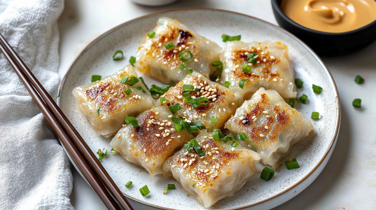 mehrere Reispapier-Dumplings auf einem Teller, bestreut mit Sesam und FrÃ¼hlingszwiebeln, daneben EssstÃ¤bchen und eine Schale ErdnusssoÃŸe.