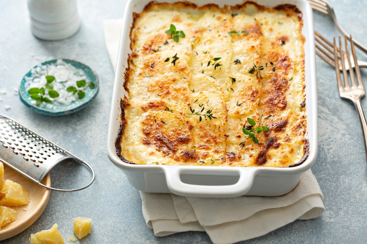 Veganes Kartoffelgratin in weiÃŸer Auflaufform, mit KrÃ¤utern bestreut, drumherum einige Zutaten.